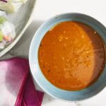 Eine Schüssel Erdnuss-Sauce auf einem Tisch, umgeben von frischen Zutaten. Ideal für gesunde Mahlzeiten und Rezepte.